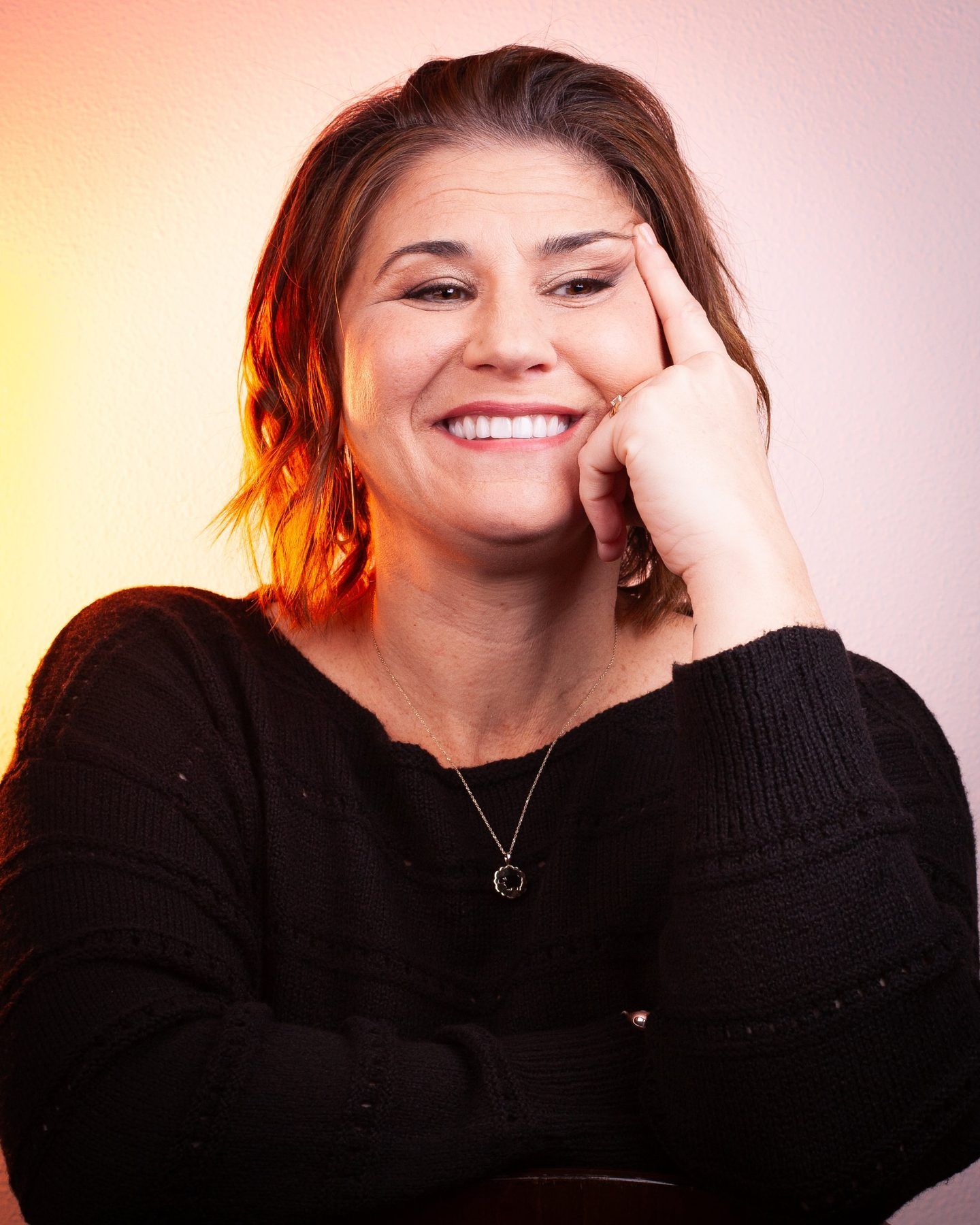 Lori Lackland laughing, fingertips at her temple, with warm amber light behind her.